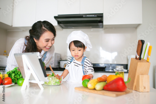 Mother with her daughter preparing lunch in the kitchen and enjoying together.