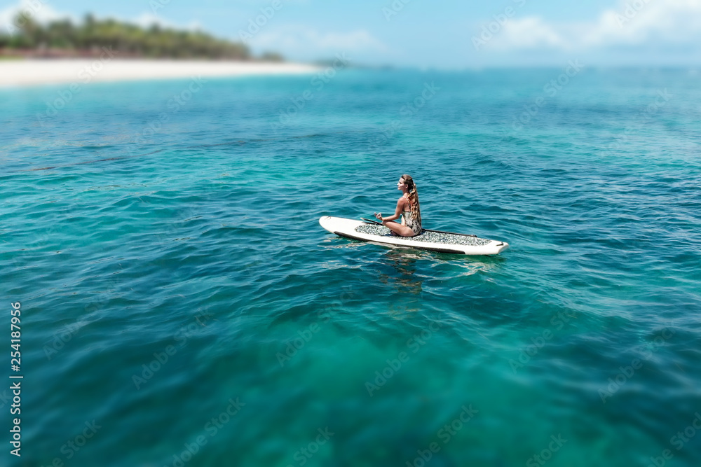 Young beautiful woman meditating in a sea at SUP paddleboarding. Healthy lifestyle. Girl in yoga pose relaxing in calm water