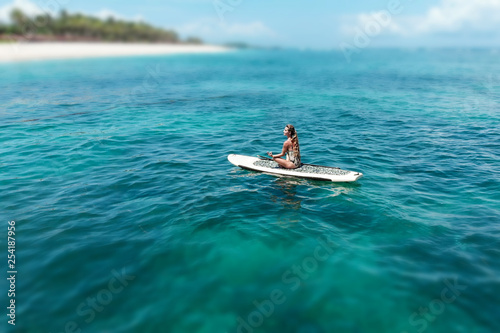 Young beautiful woman meditating in a sea at SUP paddleboarding. Healthy lifestyle. Girl in yoga pose relaxing in calm water
