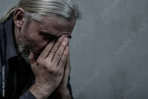 Adult man covering face and crying on dark background