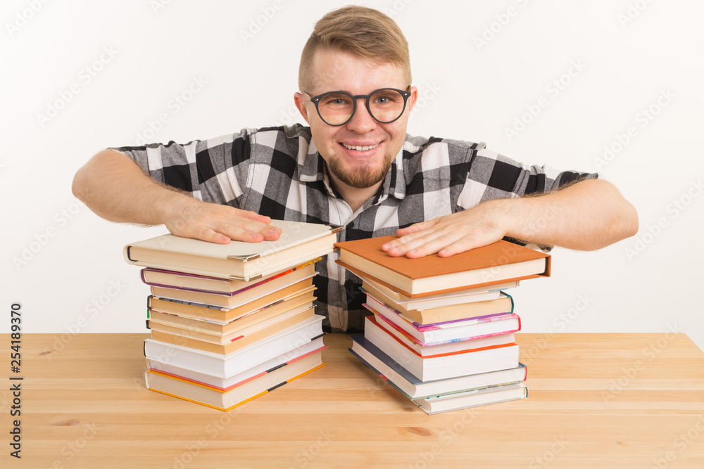 People, knowledge and education concept - Happy funny student dressed in plaid shirt sitting at the wooden table with books People, knowledge and education concept - Happy funny student dressed in plaid shirt sitting at the wooden table with books