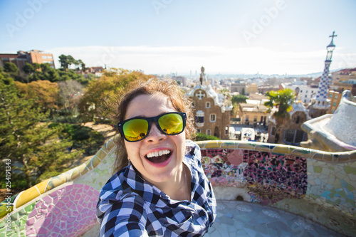 Travel and holidays concept - Beautiful young woman looking at camera taking photo with smart phone smiling in Park Guell, Barcelona, Spain.