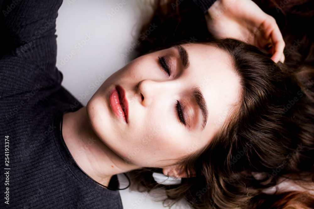 Beautiful model with long curly hair and make-up posing lying down with eyes closed Beautiful model with long curly hair and make-up posing lying down with eyes closed