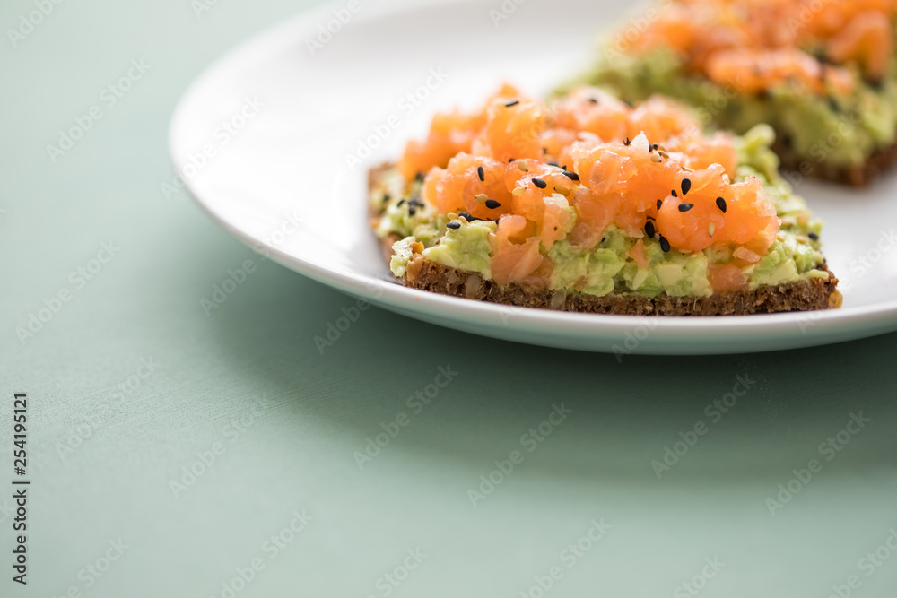 Avocado Räucherlachs Vollkorn Sonnenblumenkern Brot und Sesam zum Frühstück auf grünen Hintergrund Avocado Räucherlachs Vollkorn Sonnenblumenkern Brot und Sesam zum Frühstück auf grünen Hintergrund