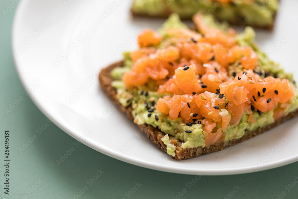 Avocado Räucherlachs Vollkorn Sonnenblumenkern Brot und Sesam zum Frühstück auf grünen Hintergrund Avocado Räucherlachs Vollkorn Sonnenblumenkern Brot und Sesam zum Frühstück auf grünen Hintergrund