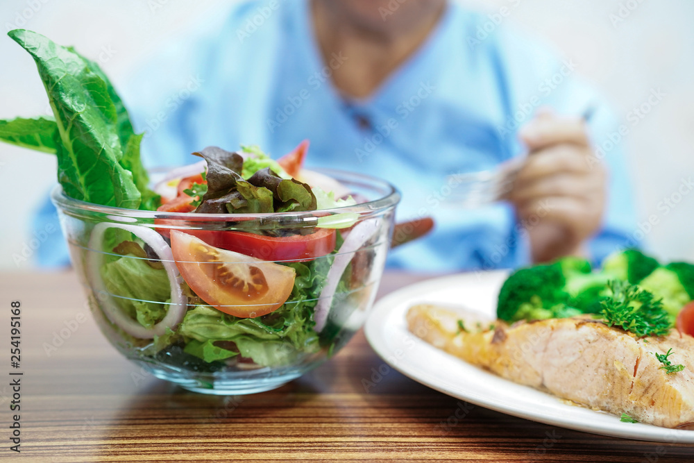 Asian senior or elderly old lady woman patient eating salmon salad vegetable breakfast healthy food with hope and happy while sitting and hungry on bed in hospital. Asian senior or elderly old lady woman patient eating salmon salad vegetable breakfast healthy food with hope and happy while sitting and hungry on bed in hospital.
