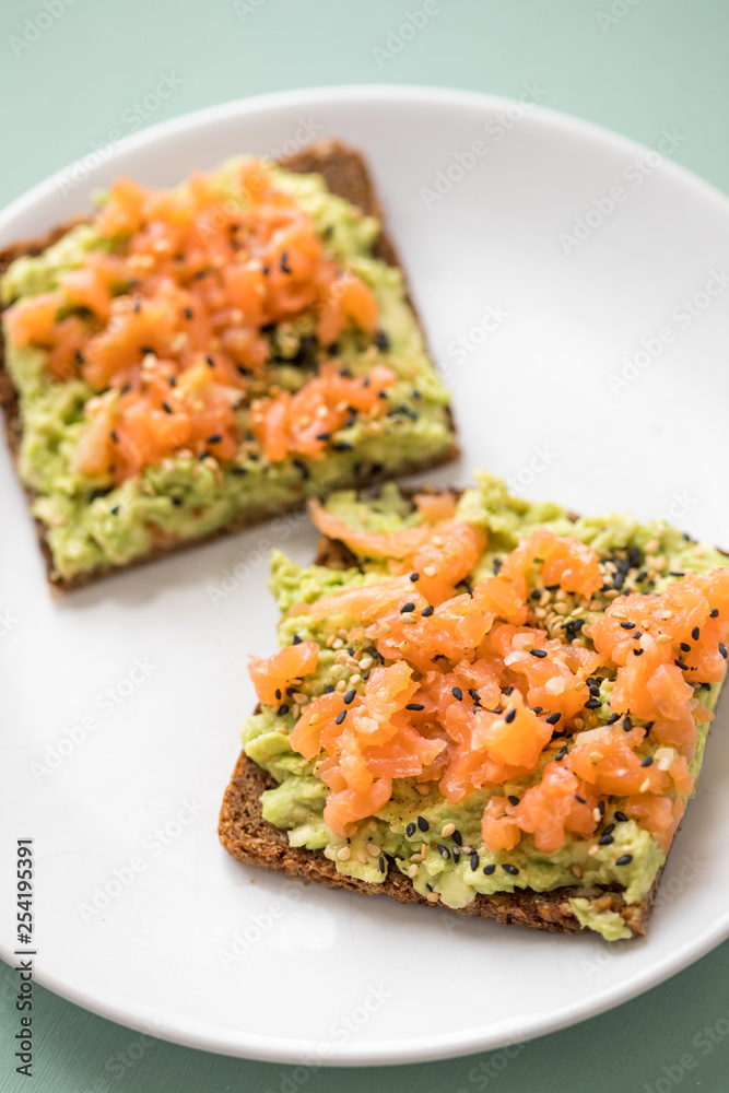 Avocado Räucherlachs Vollkorn Sonnenblumenkern Brot und Sesam zum Frühstück auf grünen Hintergrund Avocado Räucherlachs Vollkorn Sonnenblumenkern Brot und Sesam zum Frühstück auf grünen Hintergrund