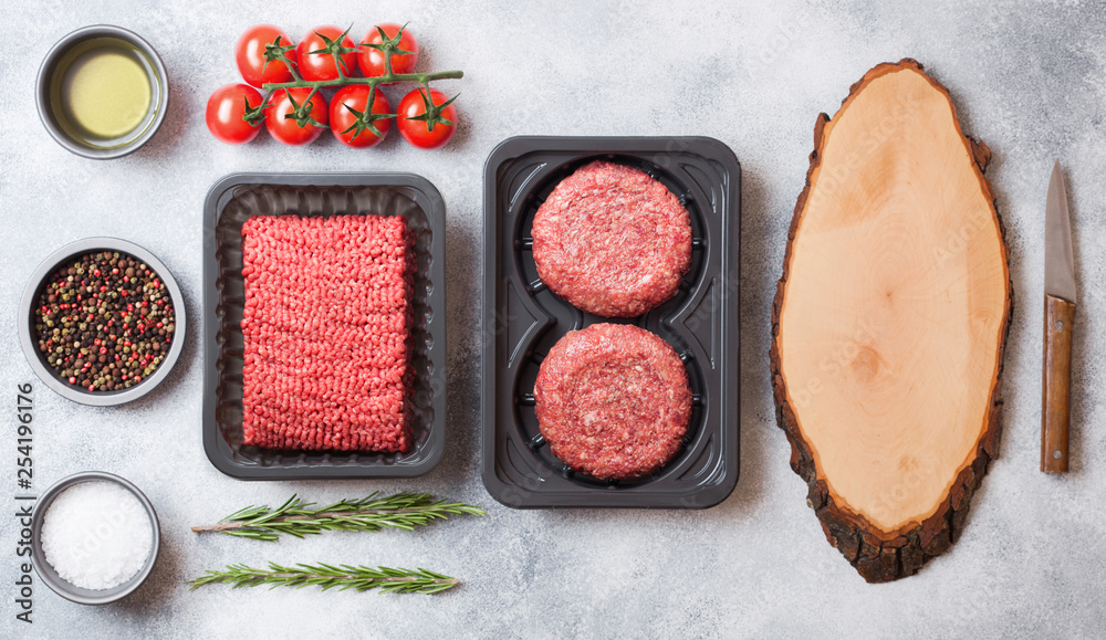 Tray with raw minced homemade beef meat with spices and herbs. Top view. On top of kitchen table background. With chopping board and knife and raw burgers. Tray with raw minced homemade beef meat with spices and herbs. Top view. On top of kitchen table background. With chopping board and knife and raw burgers.