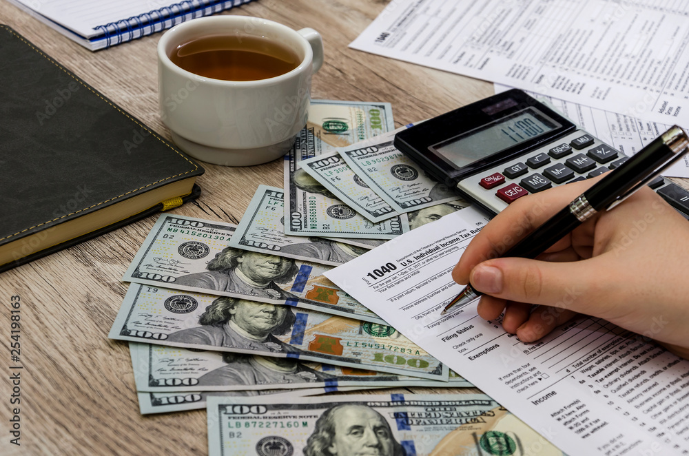the female hand fills the tax forms 1040 on a wooden table the female hand fills the tax forms 1040 on a wooden table