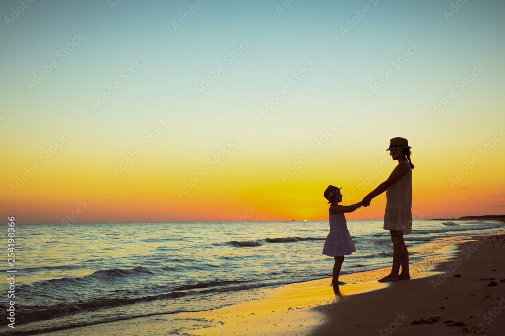 mother and daughter on ocean shore at sunset having fun time