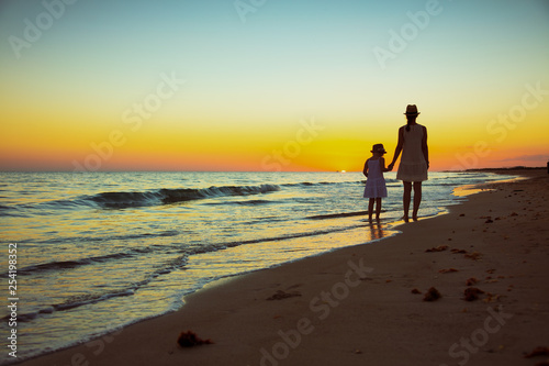 mother and daughter tourists on ocean coast at sunset walking