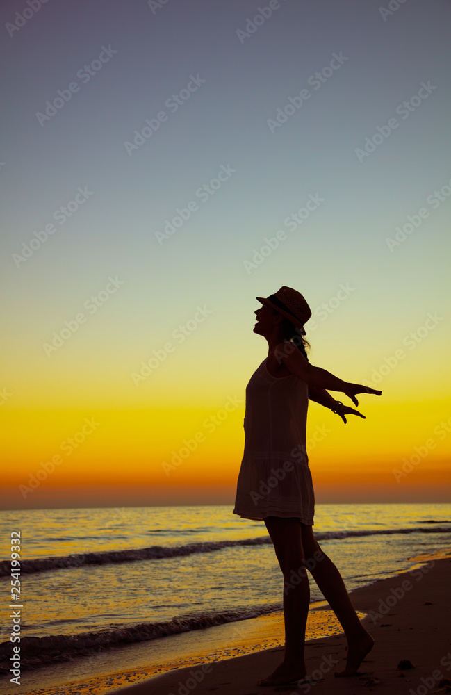 young woman on seashore at sunset rejoicing