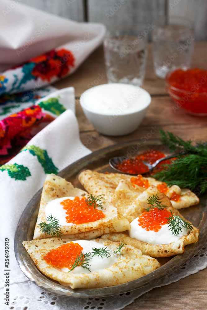 Homemade pancakes with red caviar, sour cream and dill served with vodka. Rustic style. Homemade pancakes with red caviar, sour cream and dill served with vodka. Rustic style.
