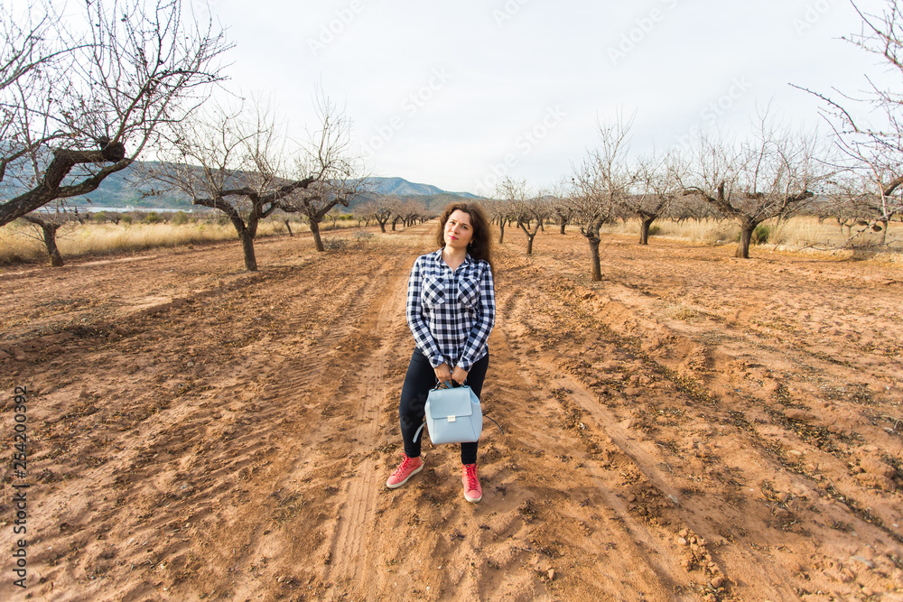 Trip, fashion and people concept - happy young woman walking with small bag and smiling over the nature