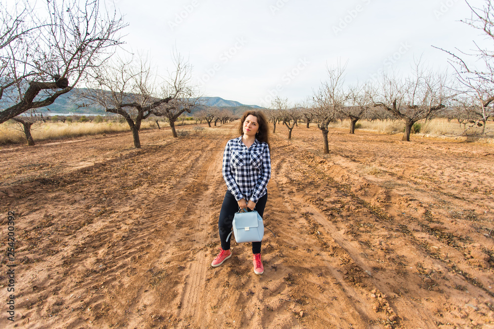 Trip, fashion and people concept - happy young woman walking with small bag and smiling over the nature Trip, fashion and people concept - happy young woman walking with small bag and smiling over the nature