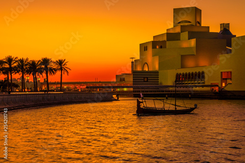 Fototapeta Naklejka Na Ścianę i Meble -  Scenic seafront landscape of Doha Bay Park with palm trees, dhow and famous landmark at colorful sunset sky. Urban cityscape of Doha, Qatari capital. Middle East, Arabian Peninsula in Persian Gulf.
