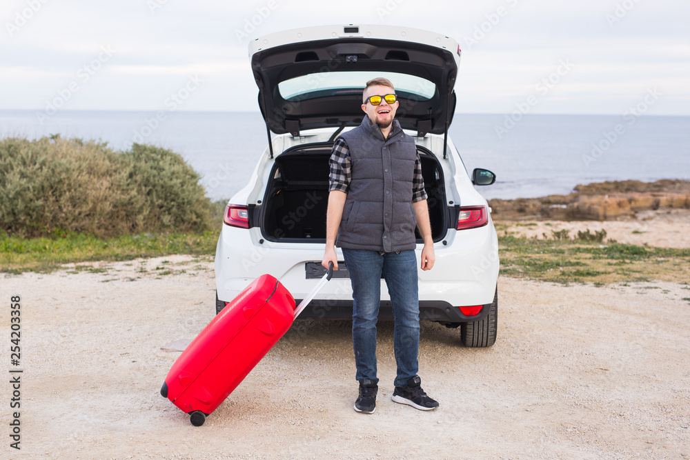Man standing in back of car smiling and getting ready to go. Young laughing mle standing near open trunk of a car. Summer road trip Man standing in back of car smiling and getting ready to go. Young laughing mle standing near open trunk of a car. Summer road trip