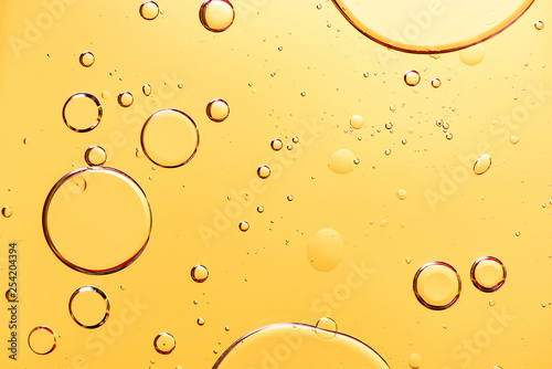 Beautiful macro photo of water droplets in oil with a yellow background.