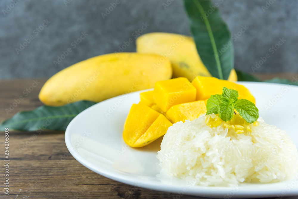 The close up of heap yellow mango and sticky rice setting with coconut milk in the dish on wooden table. popular traditional dessert of Thailand. The close up of heap yellow mango and sticky rice setting with coconut milk in the dish on wooden table. popular traditional dessert of Thailand.