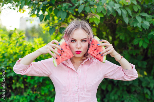 Beautiful young woman with pink hair holding two slices of watermelon in front of her face