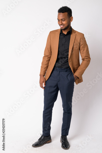 Full body shot of young happy African businessman thinking and looking down