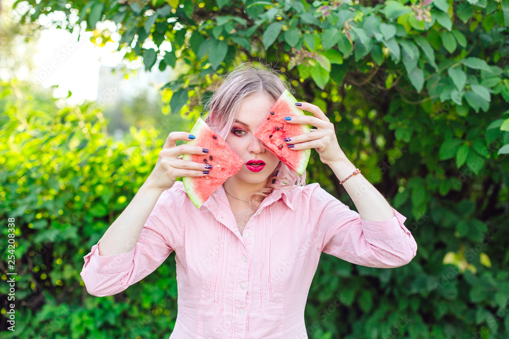 Beautiful young woman with pink hair holding two slices of watermelon in front of her face Beautiful young woman with pink hair holding two slices of watermelon in front of her face