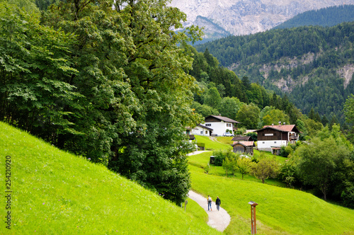 Beautiful wooded mountain slopes. Village houses in a mountain valley. Two people are walking along the road. Summer day. Austria.