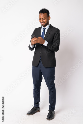 Full body shot of happy young handsome African businessman using phone