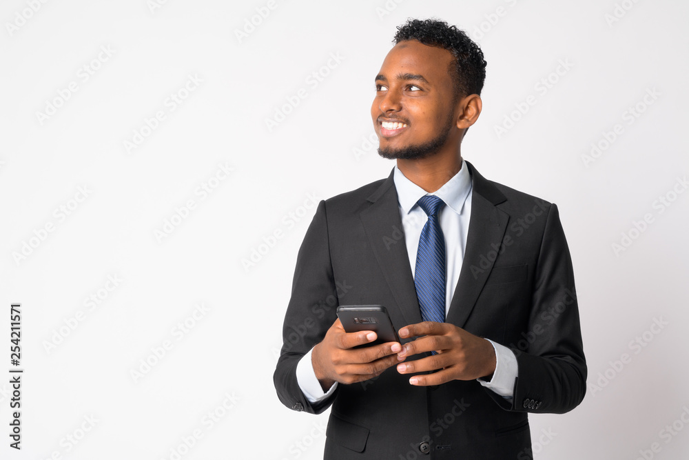 Happy young handsome African businessman thinking while using phone Happy young handsome African businessman thinking while using phone