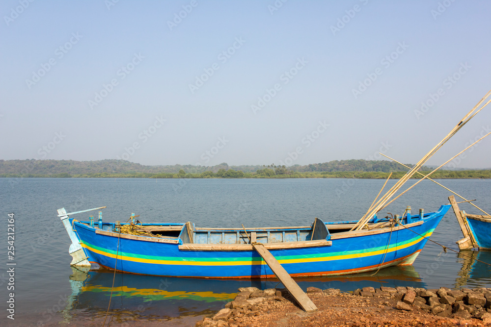 blue large fishing boat anchored near the shore against the backdrop of the river and  green forest