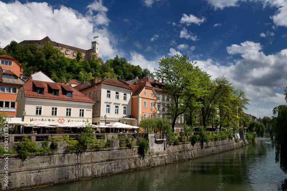 Bright pastel colors of renovated historic buildings Cankar Quay embankment of the Ljubljanica river canal and Castle Hill of Ljubjlana Slovenia