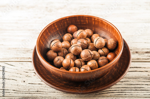 Macadamia nuts on a wooden plate on a white textural table close up and copy space