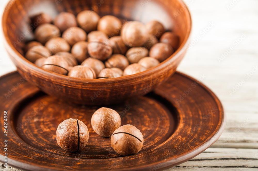 Macadamia nuts on a wooden plate on a white textural table close up and copy space Macadamia nuts on a wooden plate on a white textural table close up and copy space