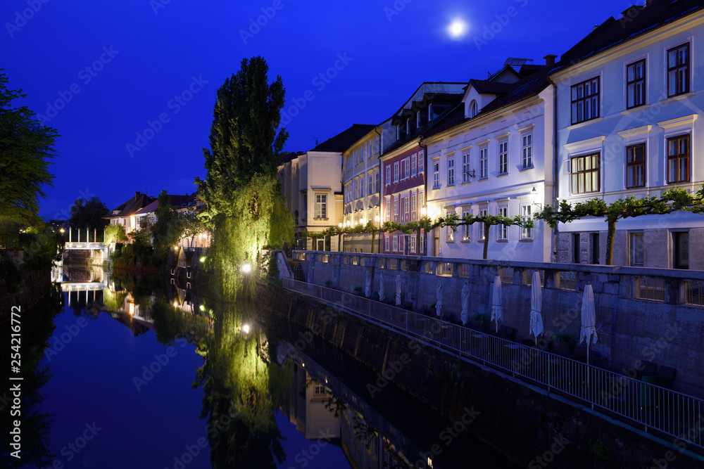 Cobblers Bridge and houses reflected on the calm Ljubljanica river canal in moonlight at dawn in Ljubljana Slovenia