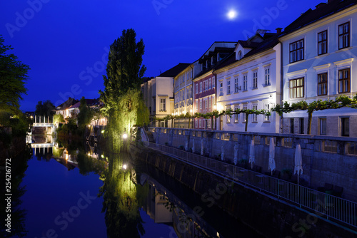 Cobblers Bridge and houses reflected on the calm Ljubljanica river canal in moonlight at dawn in Ljubljana Slovenia
