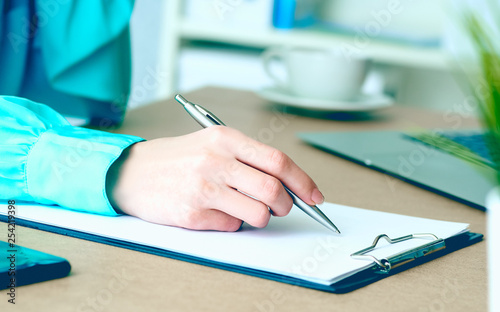 Close-up of female hands writing something in clipboard sitting at office.