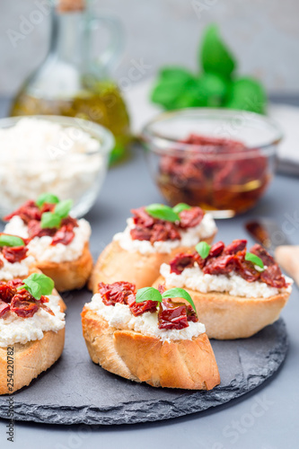 Bruschetta with sun dried tomato, feta and philadelphia cheese and basil on stone plate, vertical, closeup