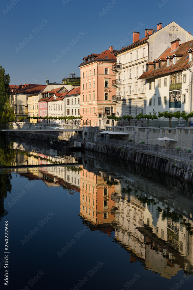 Bright buildings at the Ribja Brv modern footbridge reflected in the calm Ljubljanica river canal in Ljubljana Slovenia