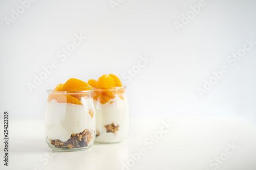 Jars of greek yogurt with granola and canned apricots on white background
