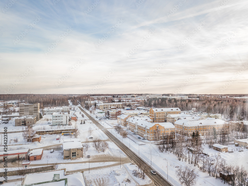 Winter landscape from a aerial view of the city of Novosibirsk in the haze with streets, small buildings, covered by snow and road crossed at the sunset wth bue sky
