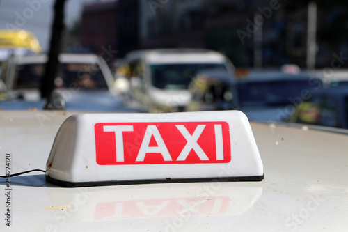 Taxi light sign or cab sign in white and red color with white text on the car roof at the street blurred background