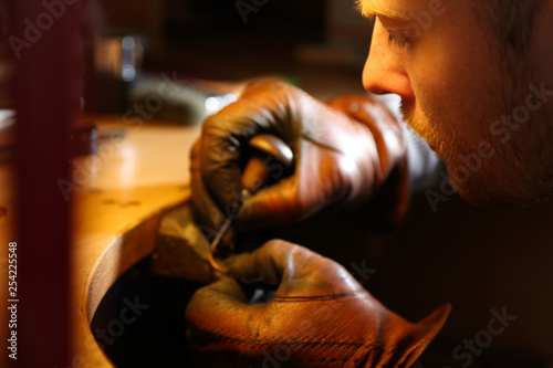 Jeweler engraving the ring with sharp with an awl in a workshop lith with warm light photo