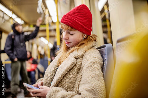 junge Frau, Mädchen, Teenager, sitzt mit ihrem Smartphone, Handy, in der U-Bahn photo