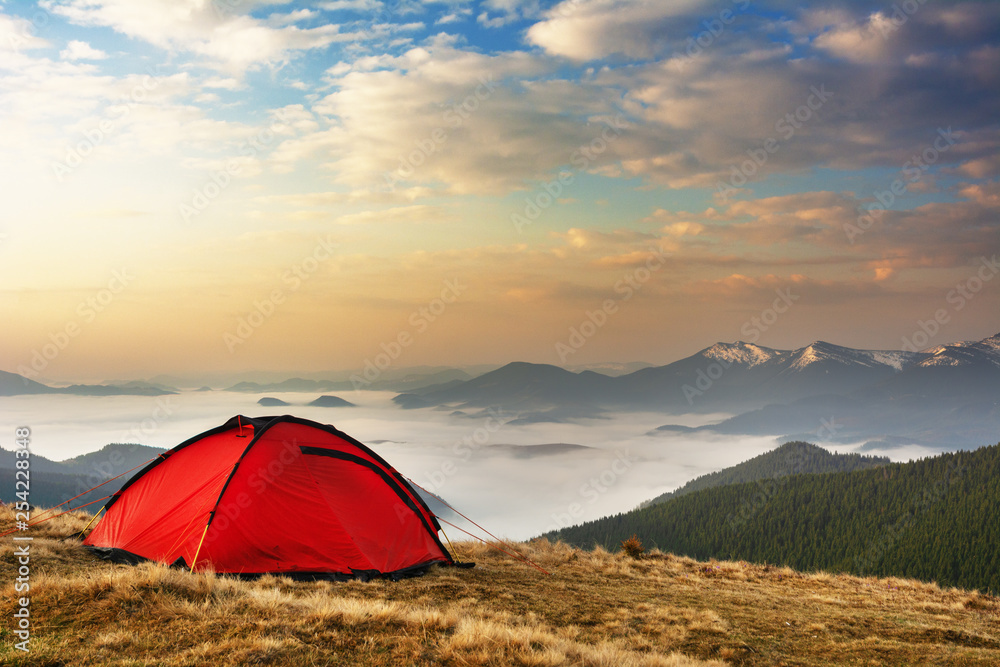 Spring on the mountainous valleys in the Ukrainian Carpathians overlooking the high snow-capped peaks covered with fogs against the backdrop of a tourist red tent