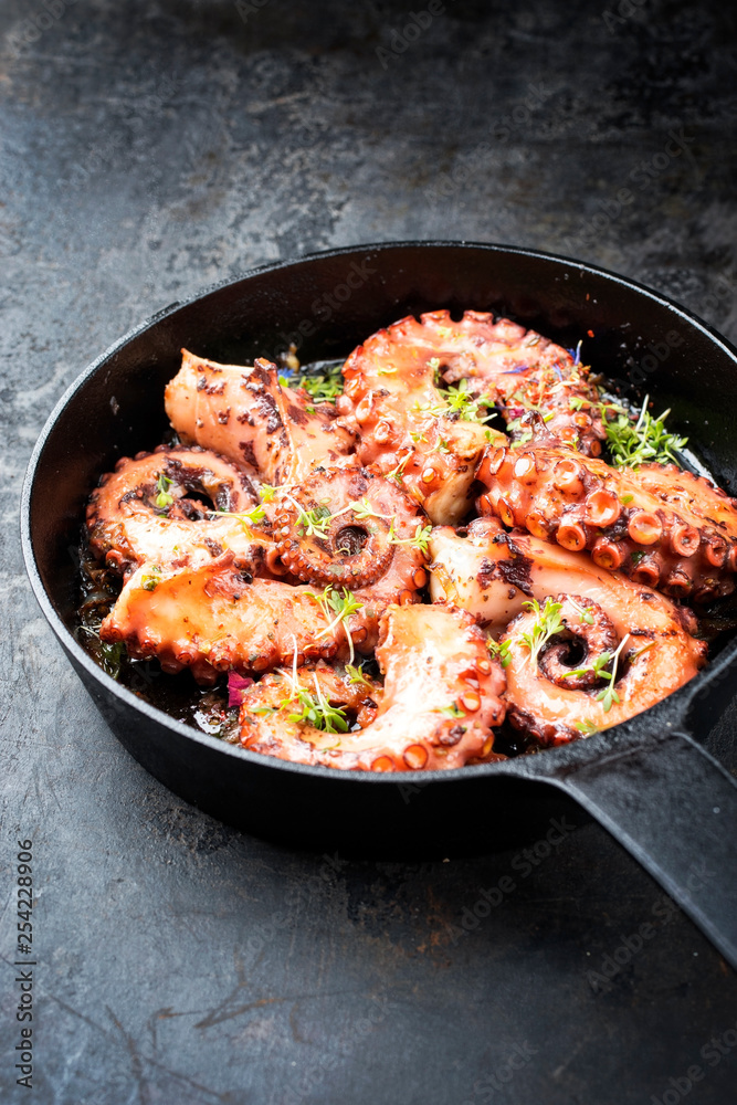 Traditionell geschmorter spanischer Oktopus mit Tomaten und Kräuter in Wein Sauce als closeup in einer gußeisernen Pfanne