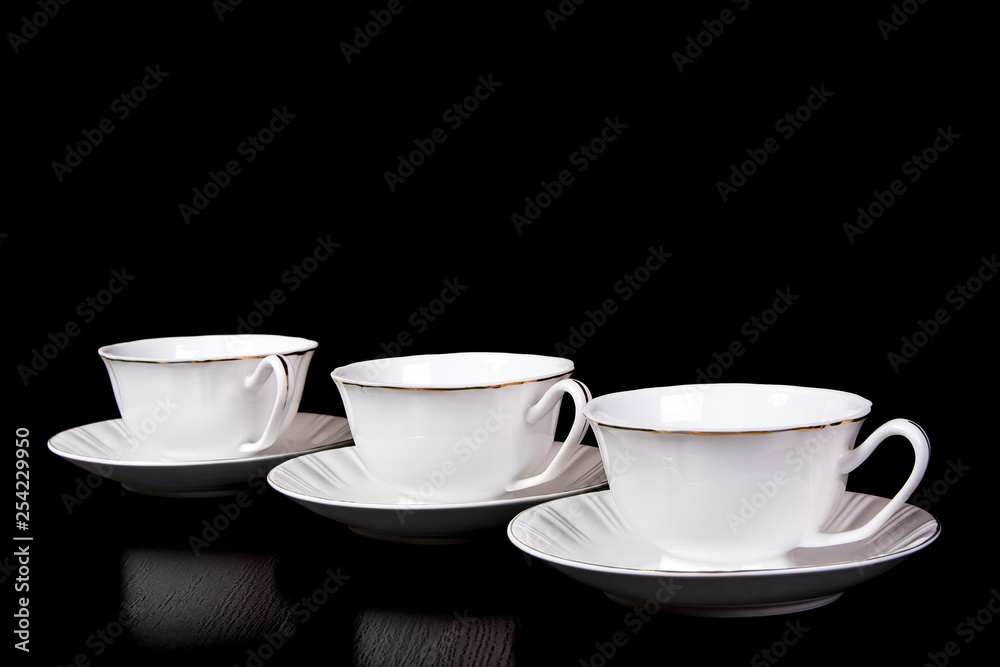 Three white tea cups in saucers stand on the table on a black background