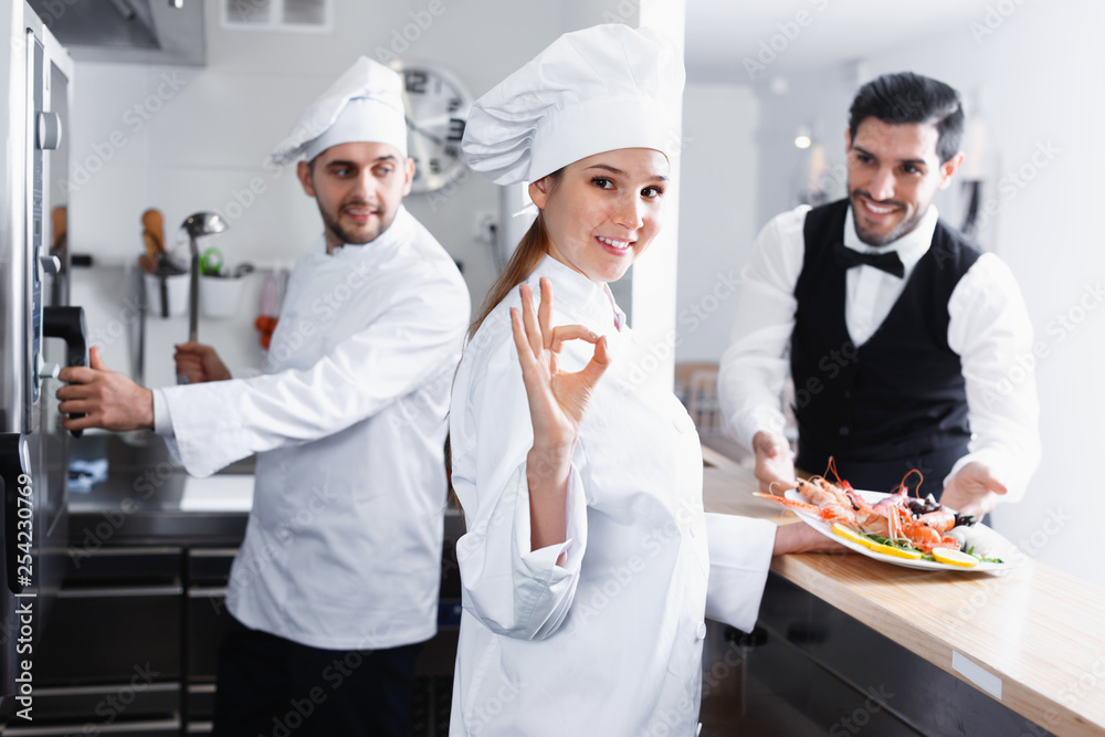 Smiling woman chef approving dish in kitchen of fish restaurant before serving guests