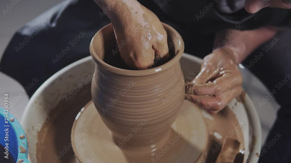 Potter creates product on potter's lathe spinning pottery. Hands gently create correctly shaped handmade from clay in slow motion Potter creates product on potter's lathe spinning pottery. Hands gently create correctly shaped handmade from clay in slow motion