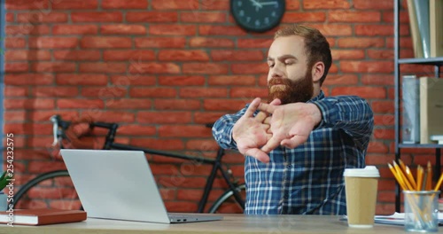 Young smiled Caucasian man with a beard stretching arms while resting during work in the office at the laptopo computer. photo