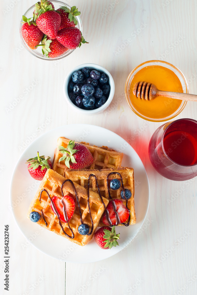 Photo of fresh homemade food made of berry Belgian waffles with honey, chocolate, strawberry, blueberry, maple syrup and cream. Healthy dessert breakfast concept with juice. Photo of fresh homemade food made of berry Belgian waffles with honey, chocolate, strawberry, blueberry, maple syrup and cream. Healthy dessert breakfast concept with juice.